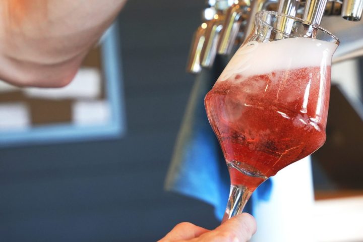 a hot pink sour beer being poured into a stemmed glass from OG bottle shop in galt