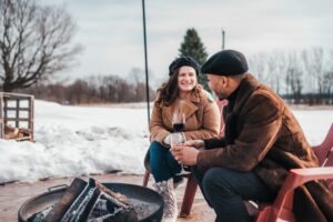 couple drinking wine at an outdoor fire pit at Burning Kiln Winery. There is snow on the ground and they are in warm winter clothes.