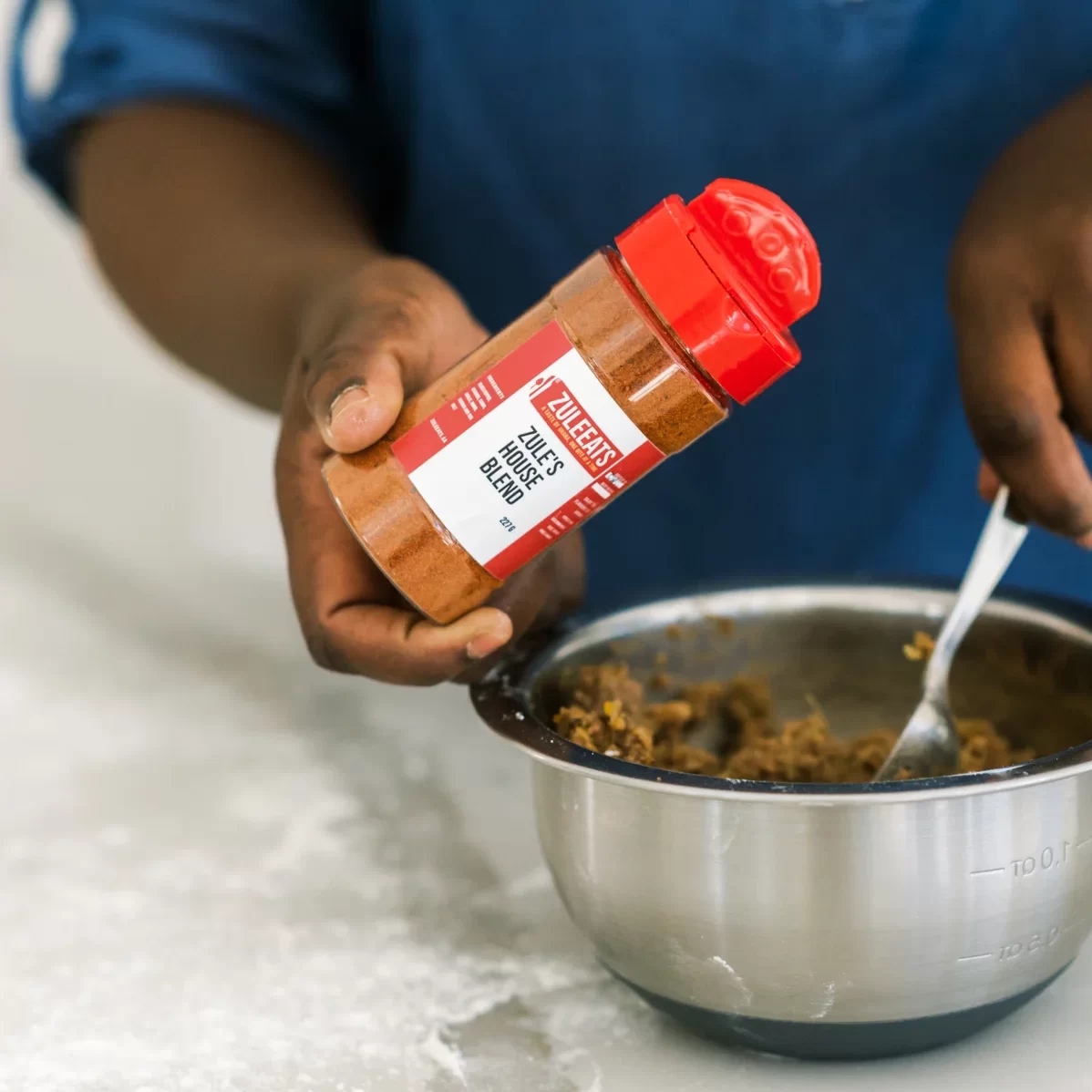 house blend seasoning from zule eats being sprinkled into a mixing bowl of food