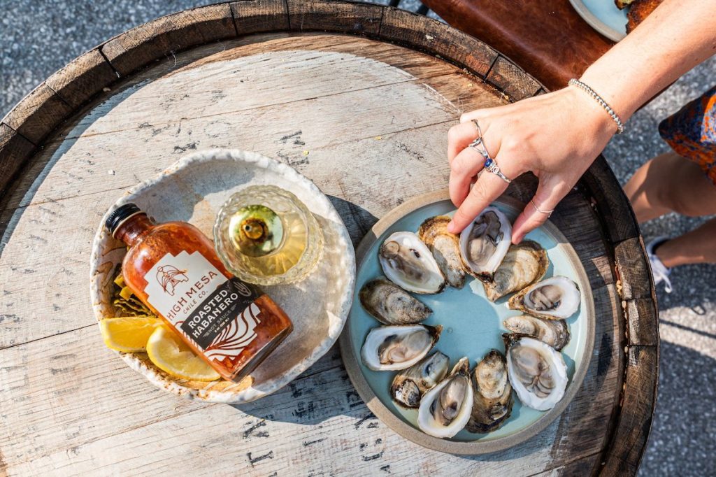 overhead shot of hand reaching into grab an oyster next to a bowl of hot sauce