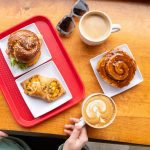 overhead shot of sticky bun, breakfast ray, breakfast sandwich and two coffees at Sweet North Bakery