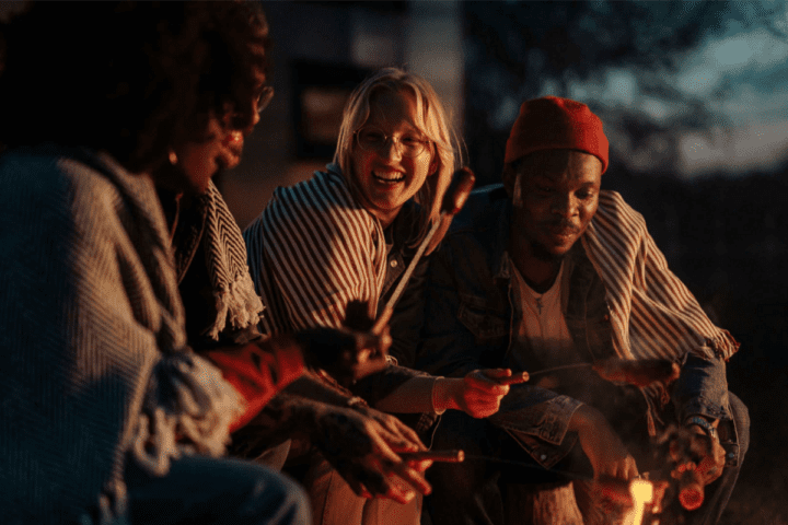 Three people by an open fire roasting hot dogs.
