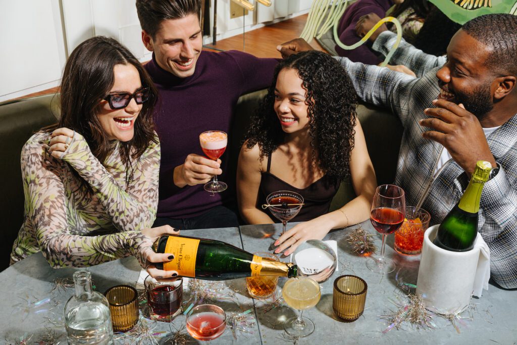 woman pouring champage for a table of four with cocktails at New Years Eve Party