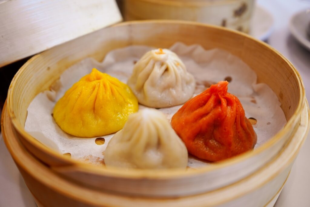 close up of dumplings in a steam basket in white, yellow and pinkish red