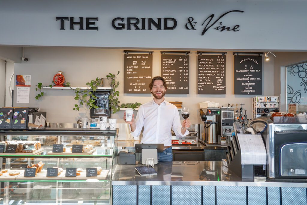 Owner holding up a coffee and a glass of wine at Grind and Vine