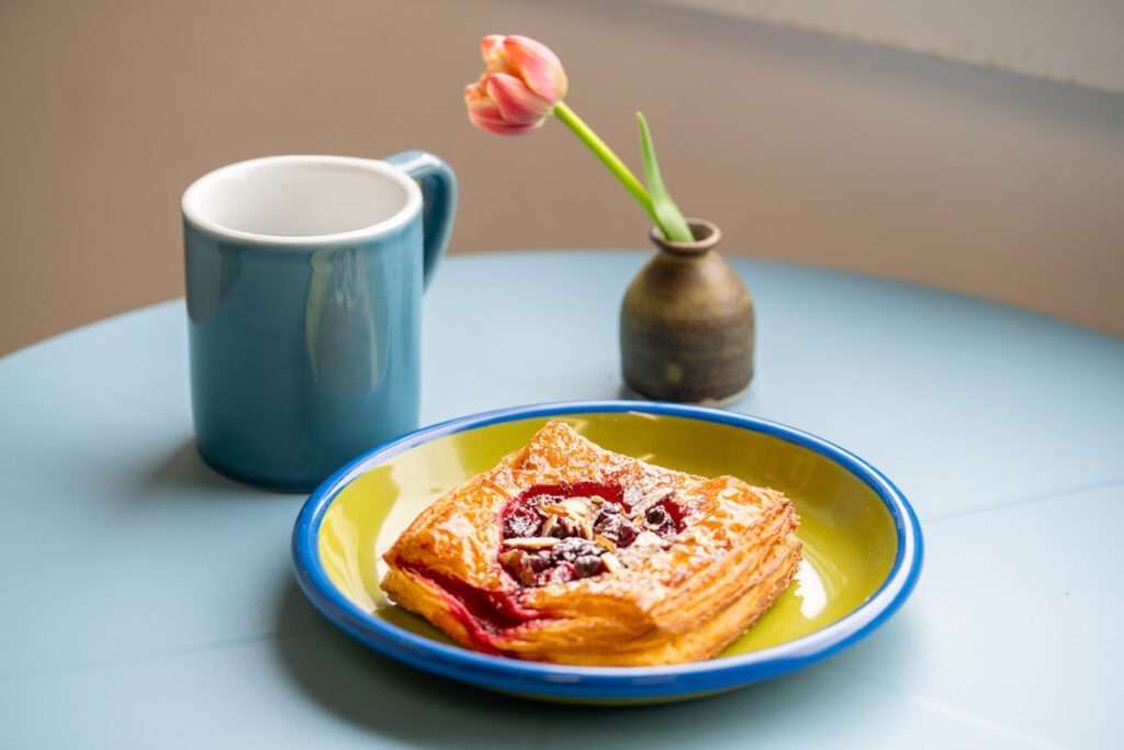 A danish, a tulip in a vase and a coffee at Small Scale Bread on a blue table