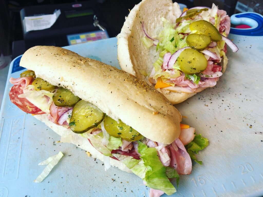 two assorted subs, one closed and one open behind it with lots of pickles