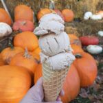 hand holding ice cream on a waffle cone in front of pumpkins