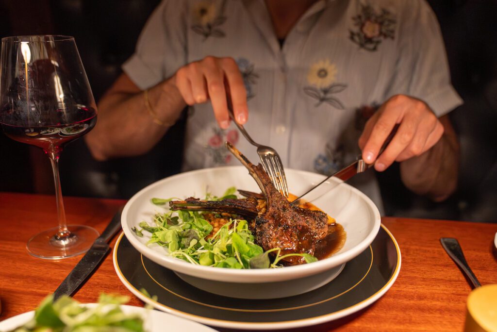 two lamb chops sitting on a bed of lettuce being cut into with a fork and knife
