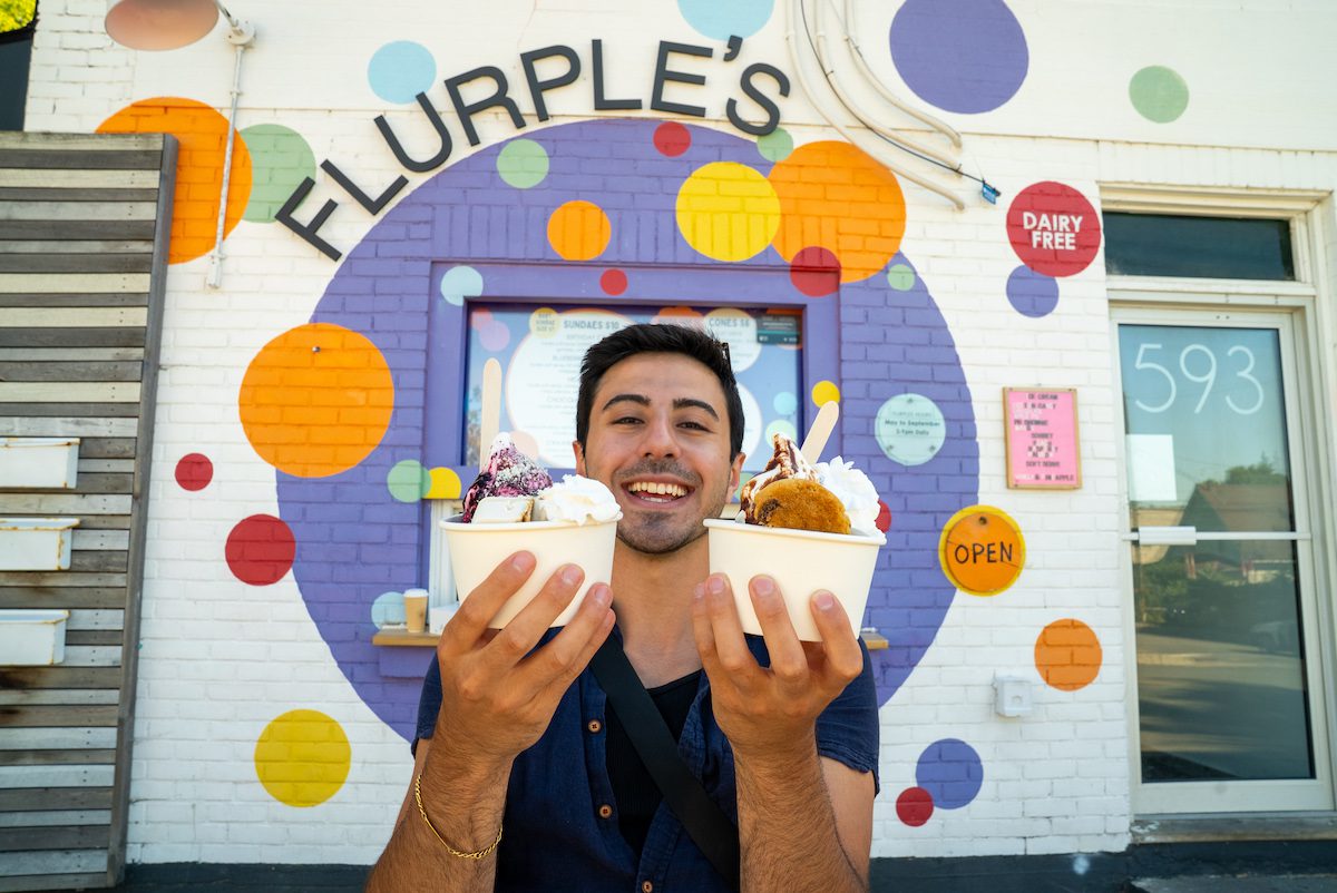 Zain holding up two bowls of ice cream at Flurple's in front of colourful mural