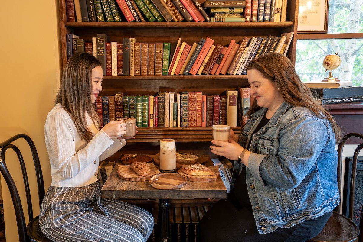 two girls drinking coffee and eating treats at Kareza Cafe in front of a bookshelf