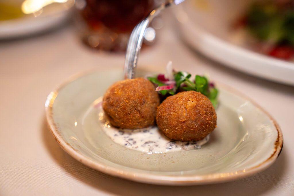 close up of two arancini on top of creamy sauce with a fork 