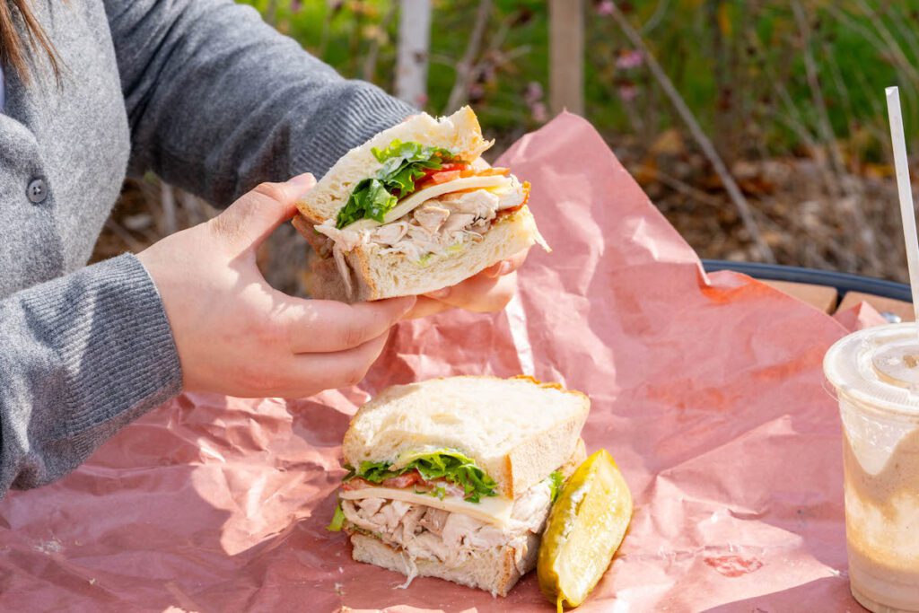 close up of hands holding a sandwich and a pickle on butcher paper