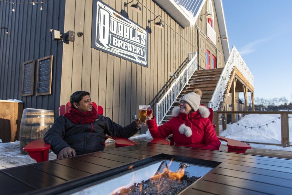 couple cheersing beer at an outdoor fire at Quayle's