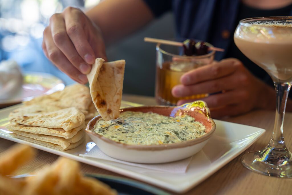 Hand dipping warm pita bread into creamy spinach and cheese dip at The Kouzzina in Sudbury.
