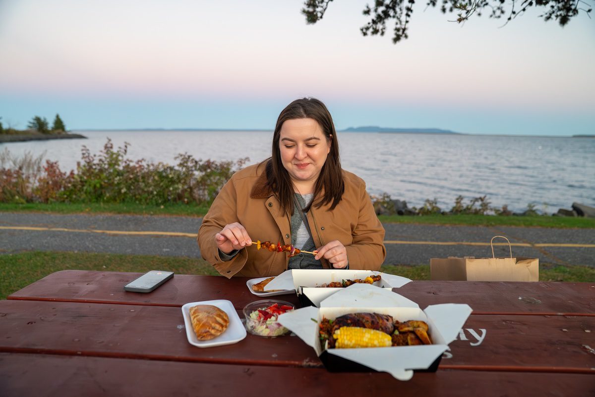 T eating food from the African Lounge on a picnic table with views of Lake Superior