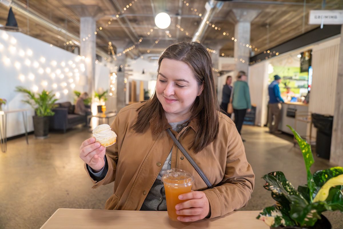 T holding a drink and a cup cake at a table at Goods and Co.