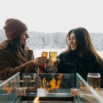 Two girls cheersing cider around a fire at an outdoor campfire