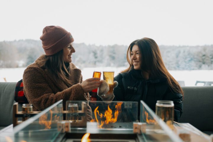 Two girls cheersing cider around a fire at an outdoor campfire