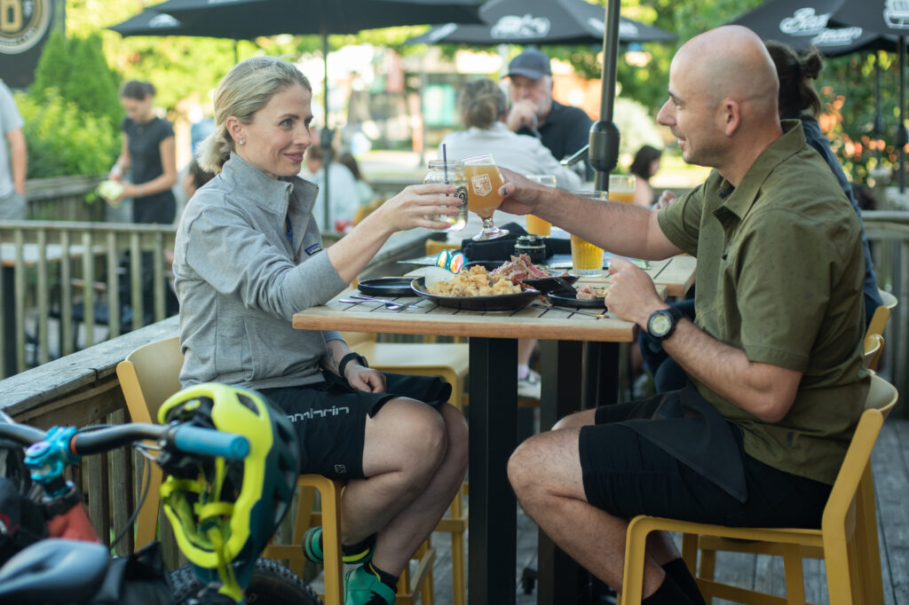 a couple in cycling gear eating a meal on a restaurant patio, a bike beside them