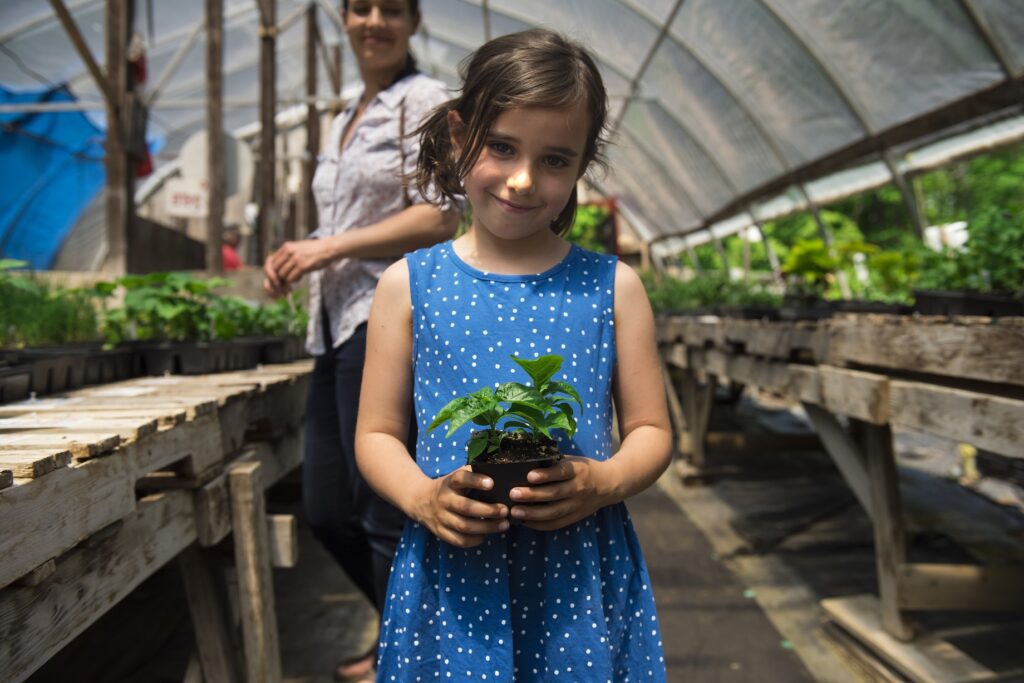 Little girl holding a plant in a greenhouse