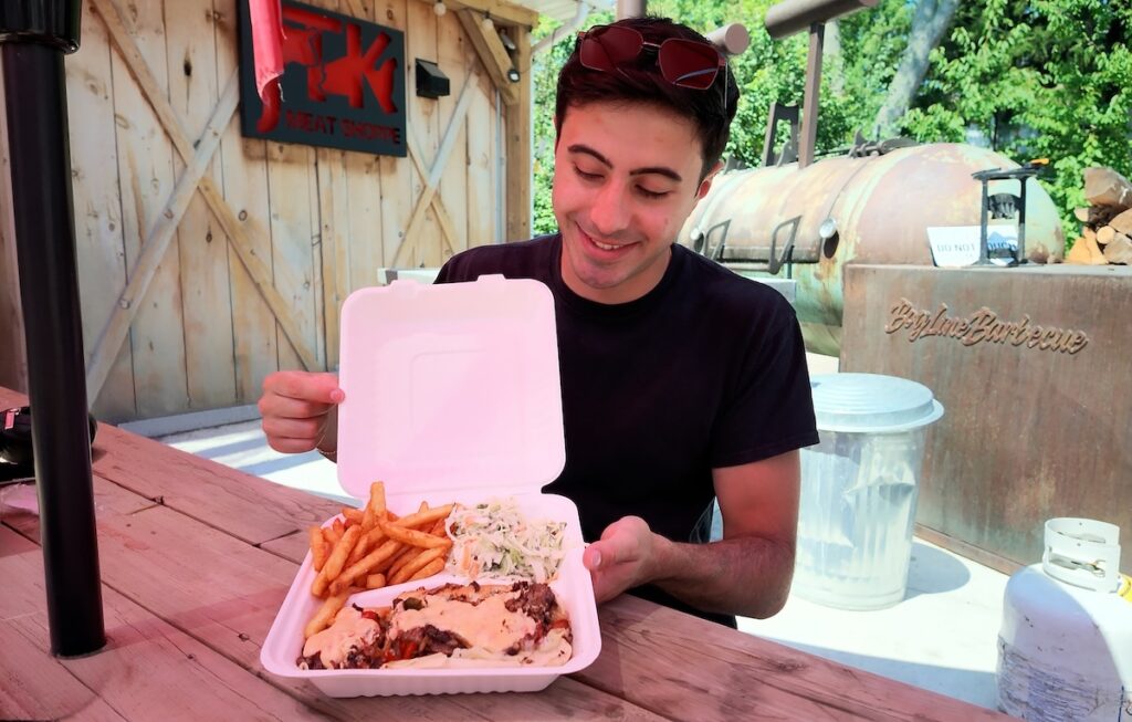 Zain showcasing his philly cheese steak and fries at a picnic table out front of JTK Meat Shoppe 