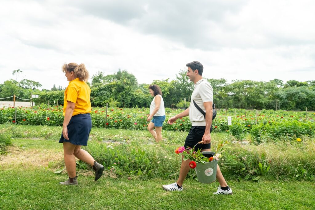 3 people walking through field with bucket of flowers