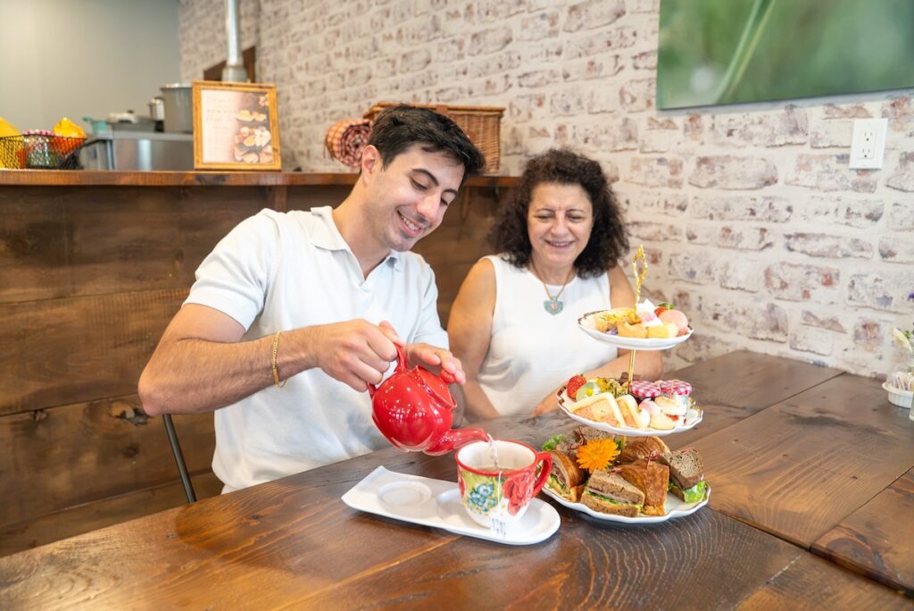 Mother and son enjoying high tea. Son pouring tea in front of a tower of sandwiches and treats.